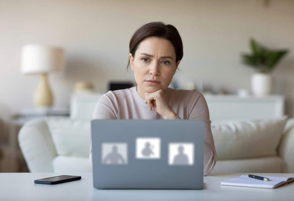 Een vrouw zit aan een bureau en kijkt bedachtzaam naar een laptop in een lichte thuiskantooromgeving.
