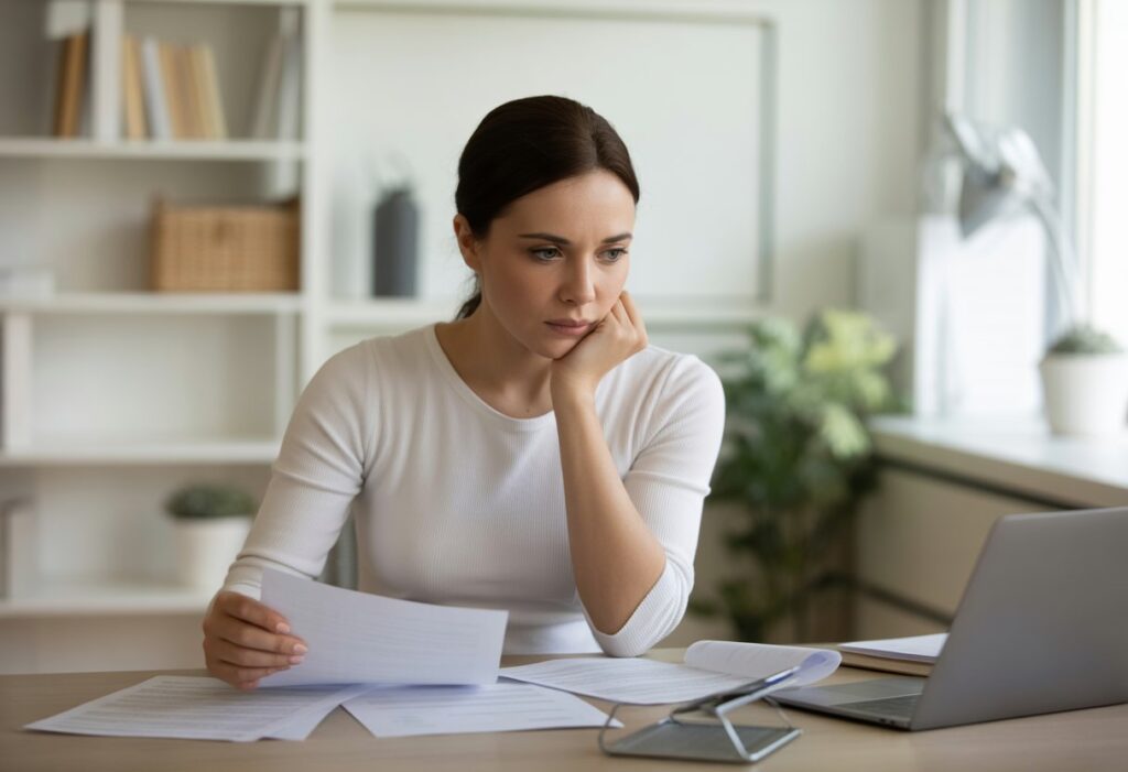 Een jonge vrouw zit aan een bureau met juridische en financiële documenten en kijkt geconcentreerd.