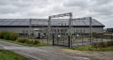 Transformatorstation langs een bedrijventerrein, met zonnepanelen op een loods erachter