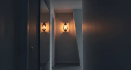 Een schemering verlichte gang met een flikkerende gaslamp aan de muur, waarvan de schaduwen de werkelijkheid vervormen — symbool voor gaslighting als vorm van psychisch huiselijk geweld.