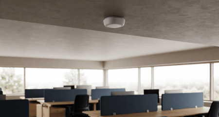 Kleine sensor aan een kantoorplafond boven werkplekken