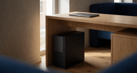 Kleine servertoren onder een bureau naast een gesloten laptop