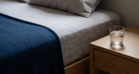 Opgemaakt bed met een opgevouwen deken en een glas water op het nachtkastje