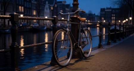 Fiets tegen een grachtenreling 's avonds onder een lantaarnpaal