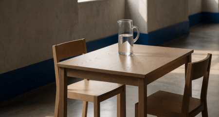 Twee stoelen aan een tafel met een karaf water in een sobere ruimte