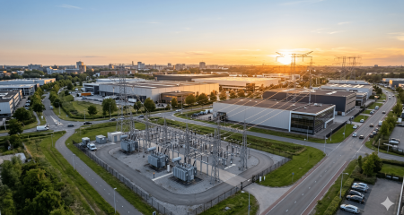Gesloten distributiesysteem met transformatorstation en hoogspanningsmasten op een industrieterrein bij zonsondergang