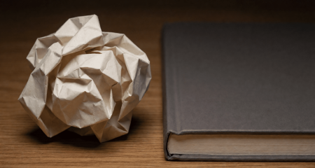 Verfrommeld papier naast een net notitieboek op een bureau