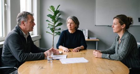 Mediator en twee partijen in gesprek aan een ovale tafel tijdens een mediation