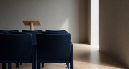 Rij lege stoelen tegenover een klein spreekgestoelte in een vergaderzaal