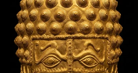 Een archeologische studiofoto van de gouden helm van Coțofenești tegen een zwarte achtergrond. De helm van gedreven goud uit de 4e eeuw v.Chr. heeft een opvallend gezichtsmasker met twee grote, gestileerde ogen en een centrale neusbeschermer. De bovenkant is bedekt met een patroon van kleine, puntige kegelvormige reliëfs, en de zijkanten zijn versierd met gedetailleerde reliëfs van dieren en spiralen. De helm rust op een strakke, donkere museumstandaard onder warme, dramatische verlichting.