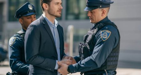 Een man wordt door een politieagent buiten een gebouw gearresteerd terwijl hij aandachtig luistert.