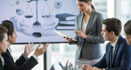 Een groep jonge professionals bespreekt juridische onderwerpen in een modern kantoor, met een vrouw die iets uitlegt op een tablet en een scherm met sociale media- en juridische symbolen op de achtergrond.