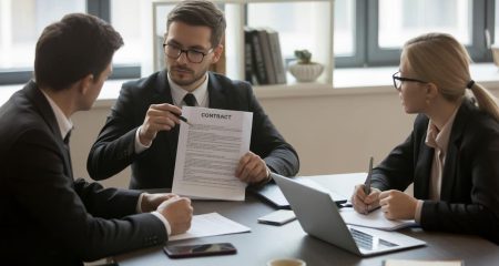 Drie professionals zitten aan een vergadertafel en bespreken een contract in een kantooromgeving.