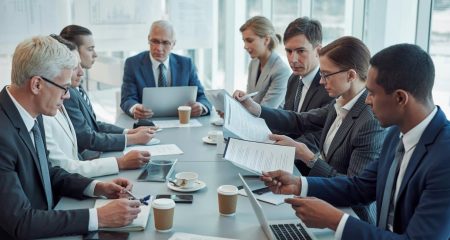 Een groep zakelijke professionals zit rond een vergadertafel in een kantoor en bespreekt documenten tijdens een formele vergadering.