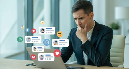 Een bezorgde professional zit aan een bureau en bekijkt een laptop met online profielen en sociale media.