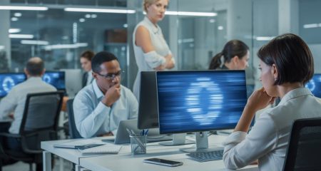 Een werknemer kijkt bezorgd naar een computerscherm terwijl een leidinggevende op de achtergrond meekijkt in een modern kantoor.