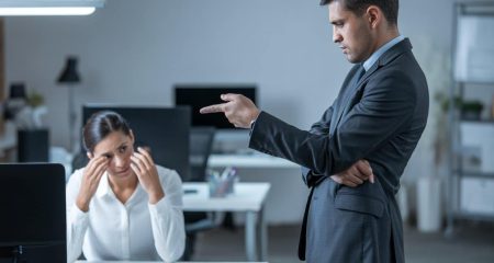 Twee collega's in een kantoor, waarbij één collega zich verdrietig en geïsoleerd voelt en de andere collega een confronterende houding aanneemt.