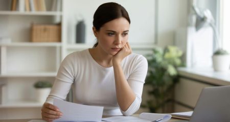 Een jonge vrouw zit aan een bureau met juridische en financiële documenten en kijkt geconcentreerd.