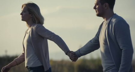 Twee volwassenen buiten, een persoon loopt weg terwijl de ander zijn arm vasthoudt en niet wil loslaten.