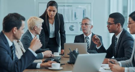 Een groep zakelijke professionals in een vergaderruimte die serieus overleggen aan een tafel met laptops en documenten.