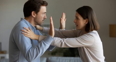 Een vrouw duwt een man met beide handen weg in een gespannen situatie binnenshuis.