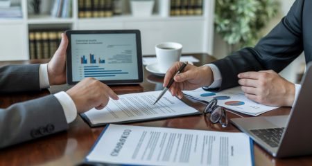 Twee zakelijke professionals bespreken contracten aan een tafel in een kantooromgeving.