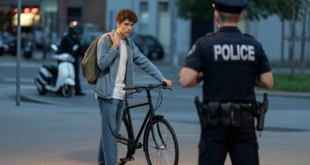 Een jonge koerier staat gespannen bij een fiets op een stadsstraat terwijl een politieagent nadert.