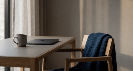 Thuiswerkplek met dichtgeklapte laptop, mok en een plaid over de stoel